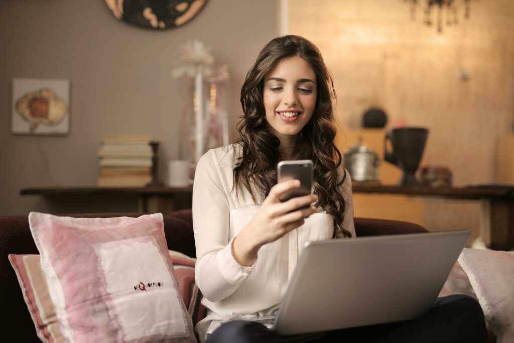 A girl using a smartphone and laptop smiling